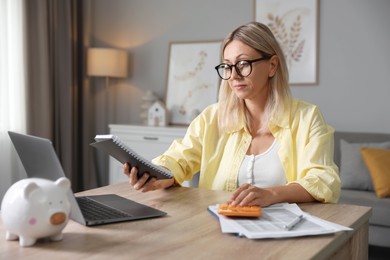 Photo of Budget planning. Woman with notebook using calculator at table indoors