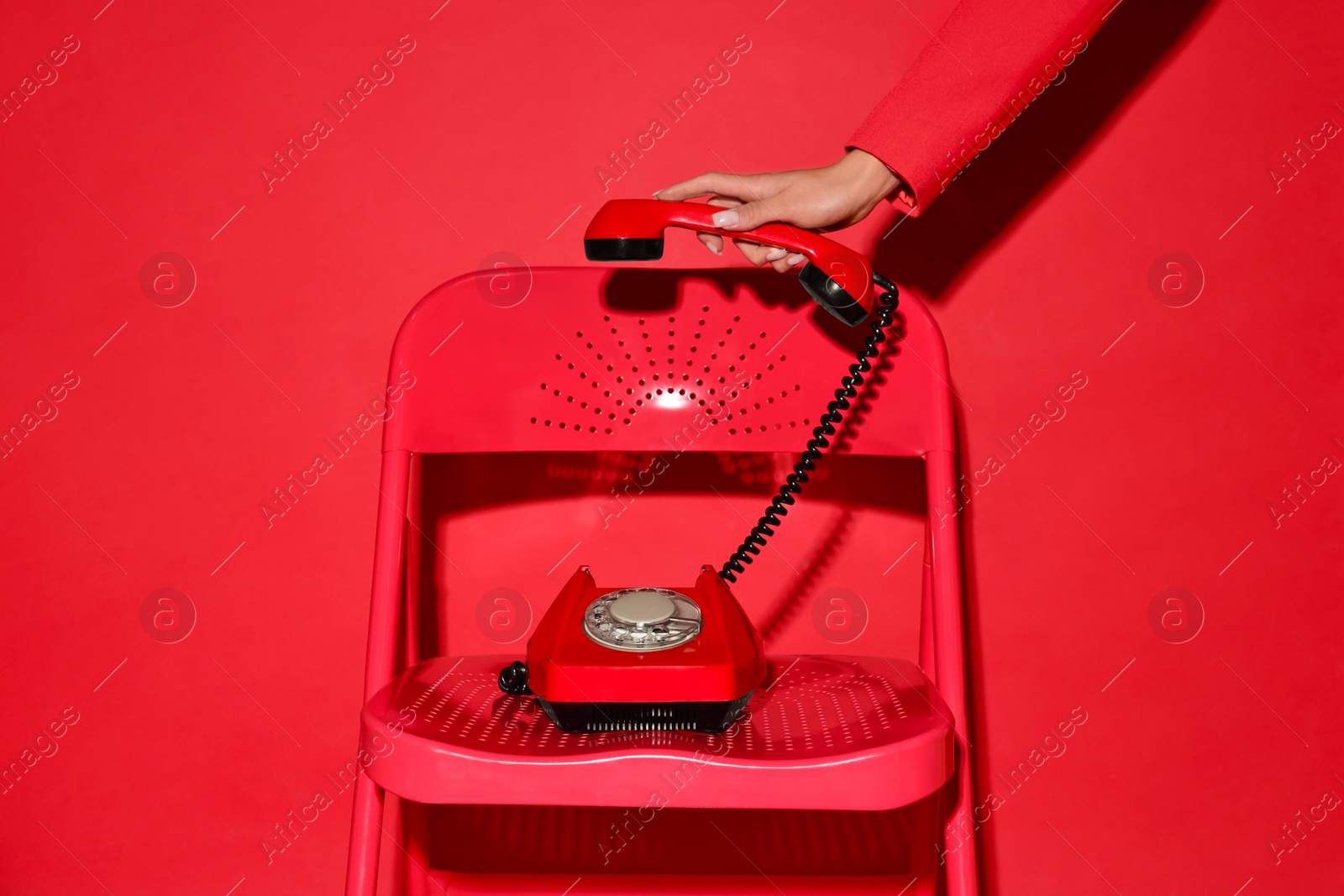 Photo of Woman with corded telephone on chair against red background, closeup