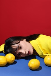 Woman with lemons at blue table on red background