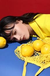 Photo of Woman with net bag and lemons at blue table on red background