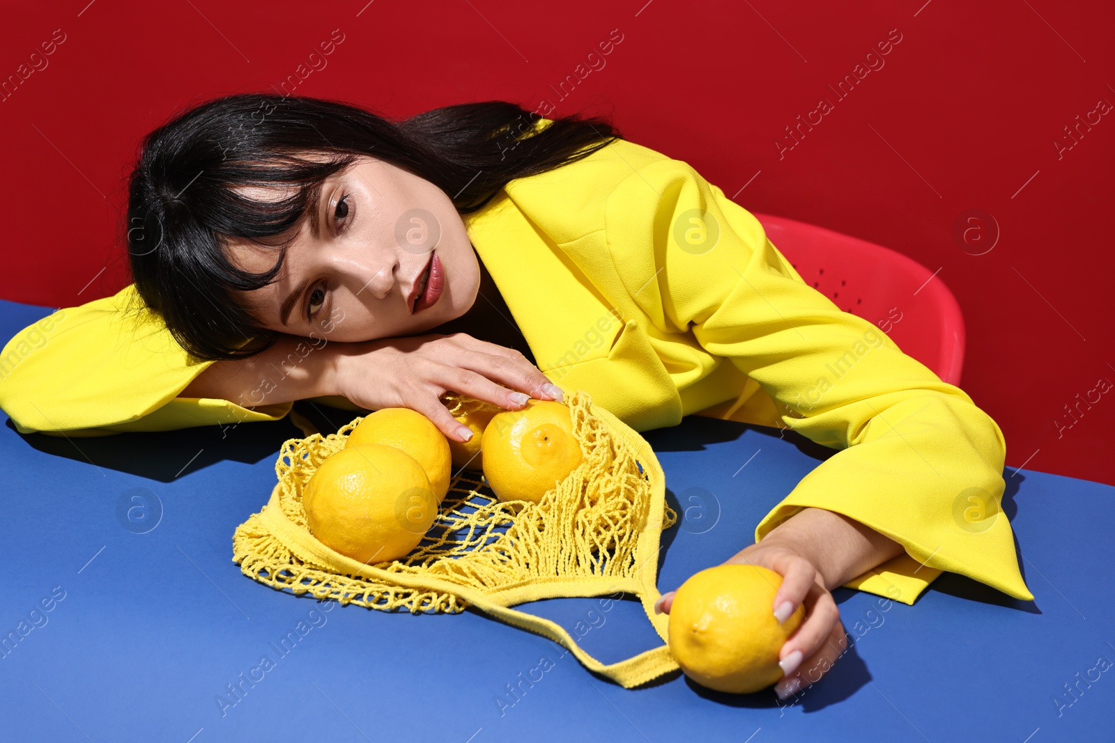 Photo of Woman with net bag and lemons at blue table on red background