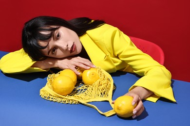 Photo of Woman with net bag and lemons at blue table on red background