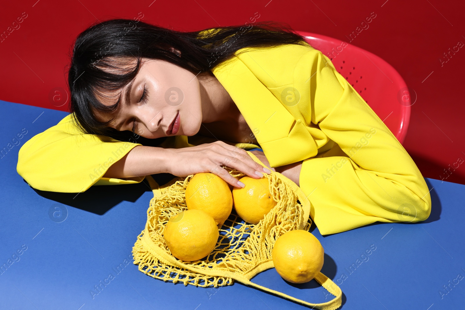 Photo of Woman with net bag and lemons at blue table on red background