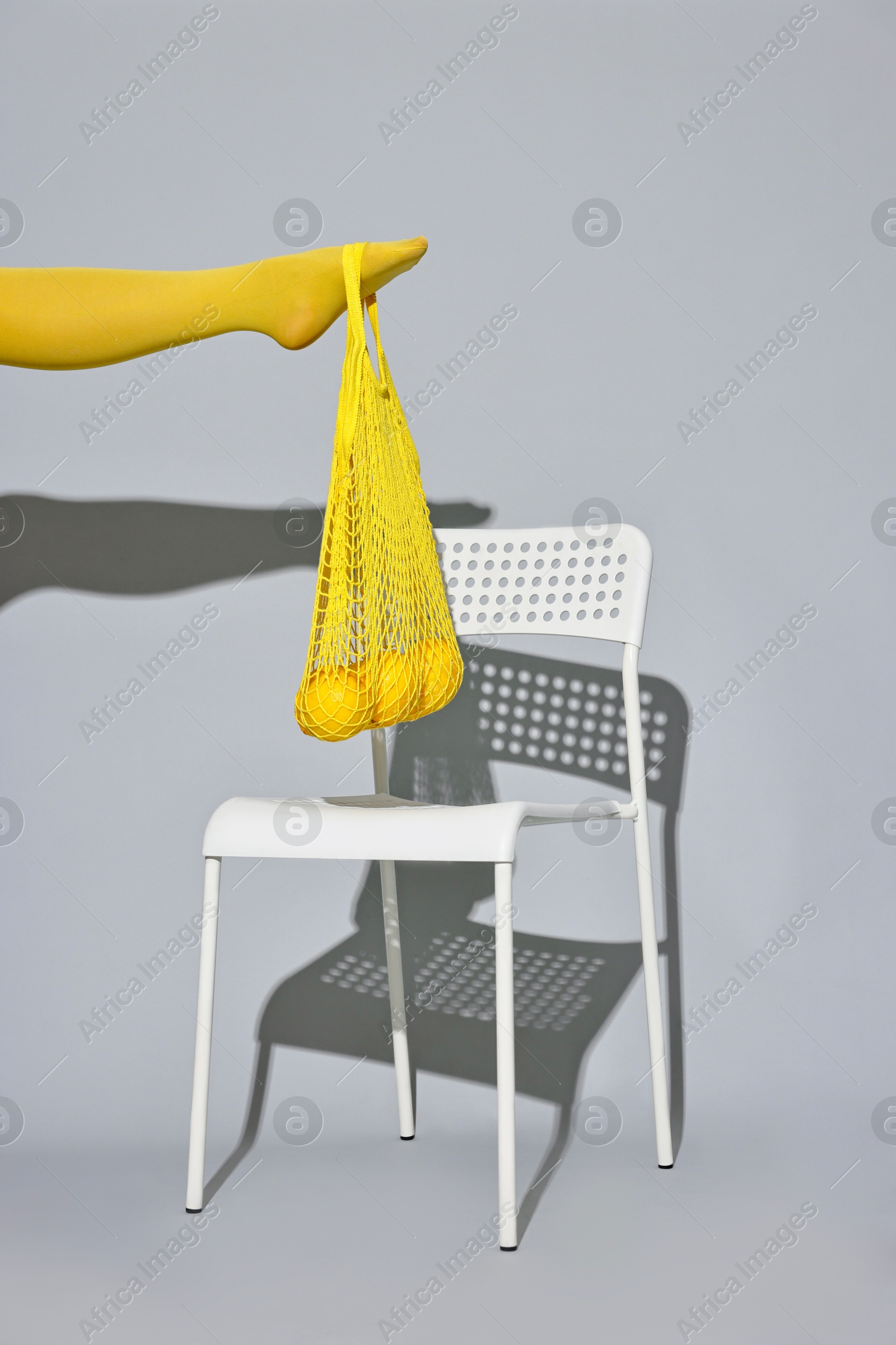 Photo of Woman with net bag and lemons on chair against light grey background, closeup