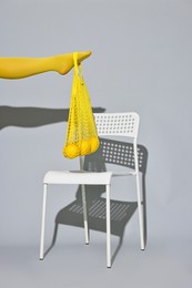 Woman with net bag and lemons on chair against light grey background, closeup