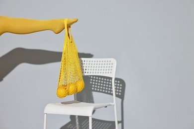 Woman with net bag and lemons on chair against light grey background, closeup