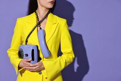 Woman in yellow jacket with corded telephone on purple background, space for text