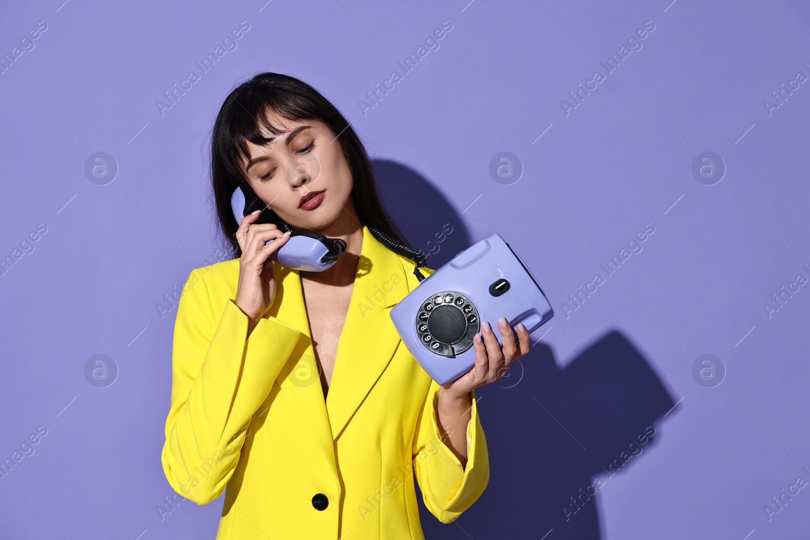 Photo of Woman in yellow jacket with corded telephone on purple background