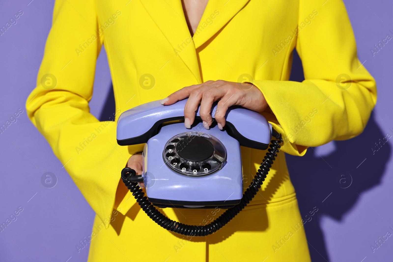 Photo of Woman in yellow jacket with corded telephone on purple background, closeup