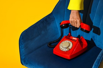 Woman with red corded telephone on blue armchair against yellow background, closeup