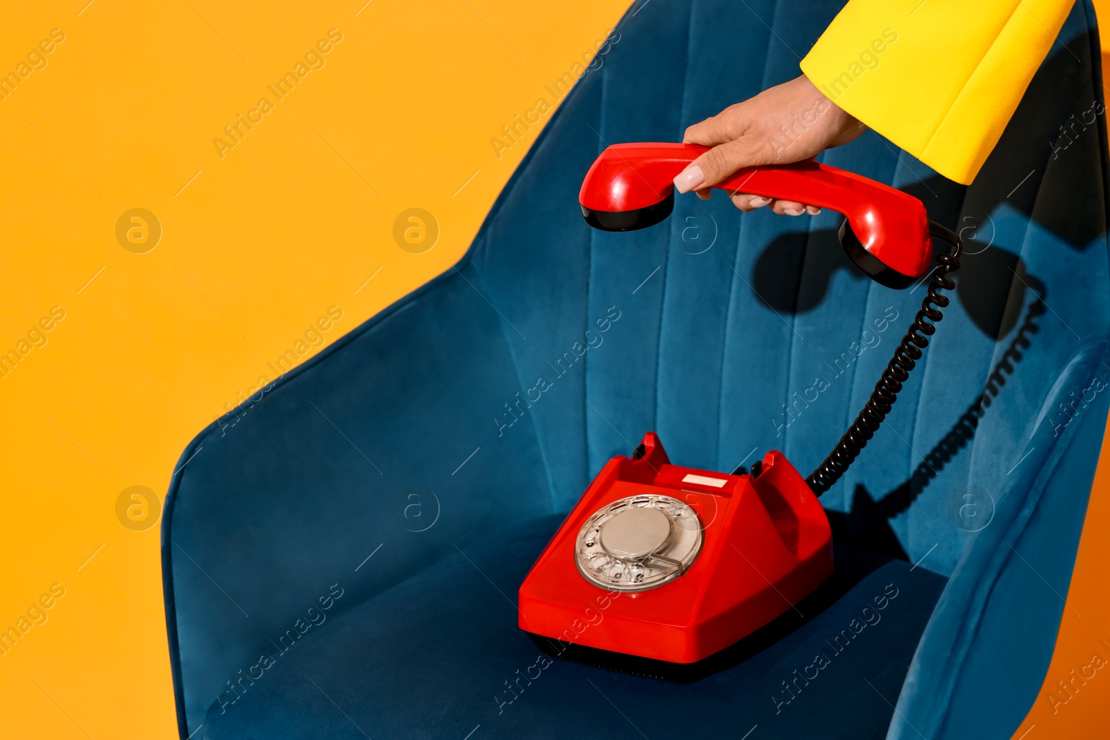 Photo of Woman with red corded telephone on blue armchair against yellow background, closeup