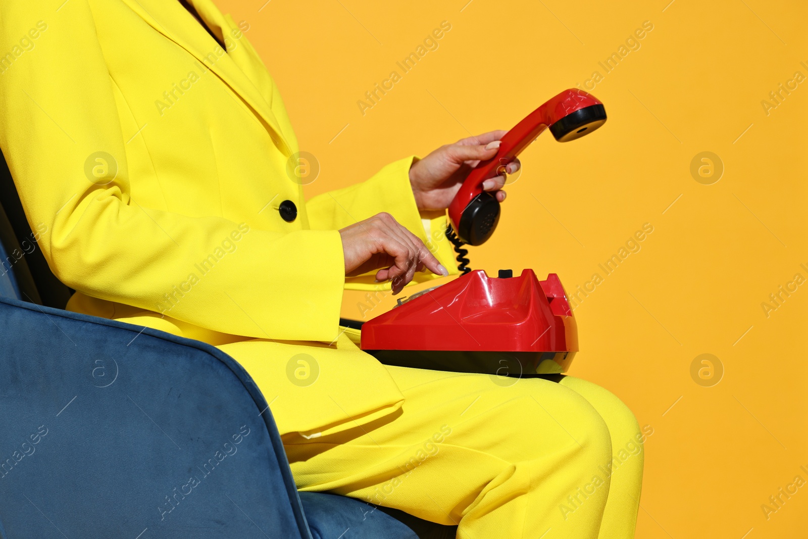 Photo of Woman with red corded telephone on blue armchair against yellow background, closeup