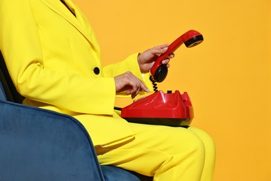 Woman with red corded telephone on blue armchair against yellow background, closeup