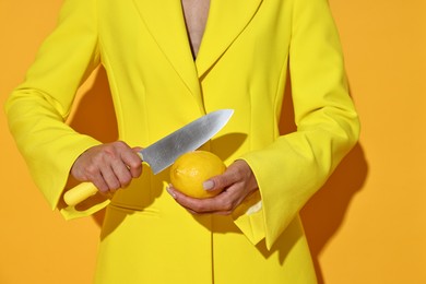 Photo of Woman with knife and lemon on yellow background, closeup