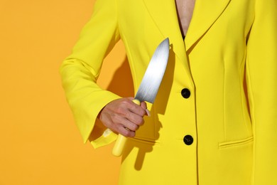 Woman with sharp knife on yellow background, closeup