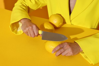 Woman with knife and lemons on yellow background, closeup