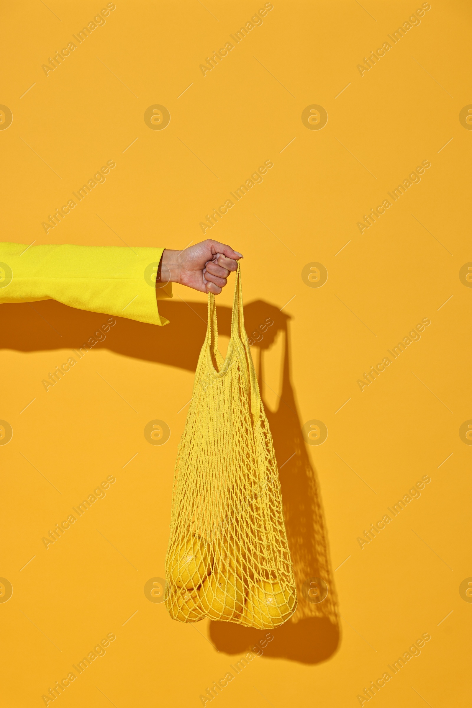 Photo of Woman with net bag and lemons on yellow background, closeup