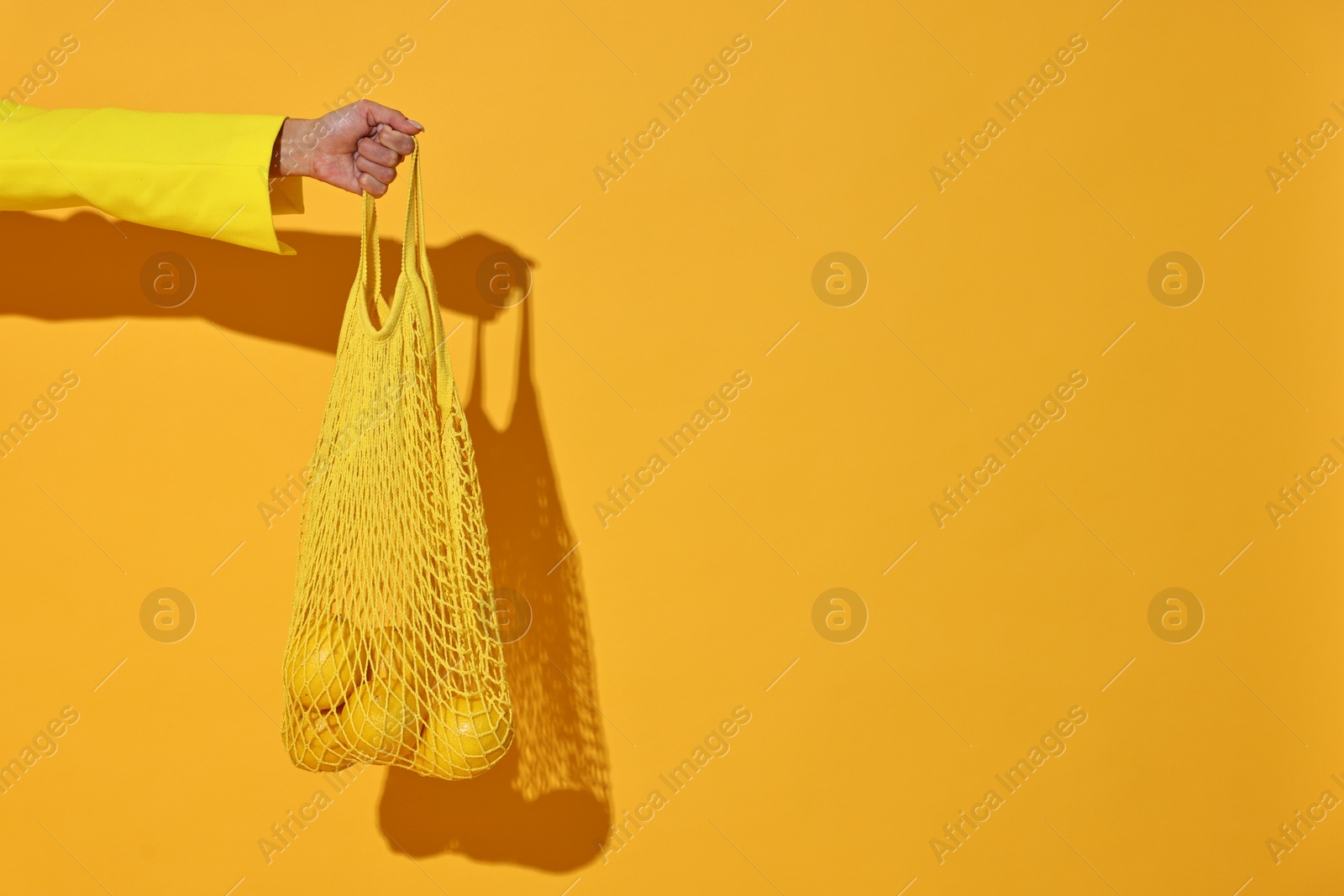 Photo of Woman with net bag and lemons on yellow background, closeup. Space for text