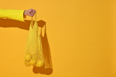 Woman with net bag and lemons on yellow background, closeup. Space for text