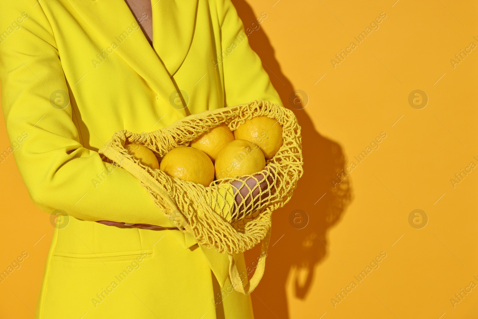 Photo of Woman with net bag and lemons on yellow background, closeup. Space for text