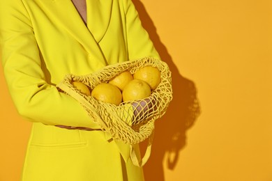 Photo of Woman with net bag and lemons on yellow background, closeup. Space for text