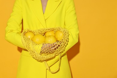 Photo of Woman with net bag and lemons on yellow background, closeup. Space for text