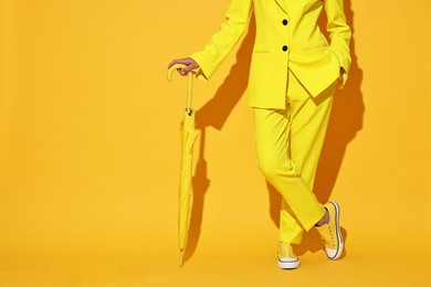 Photo of Woman with closed umbrella on yellow background, closeup. Space for text