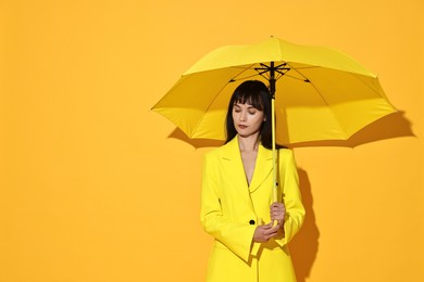 Woman with open umbrella on yellow background, space for text