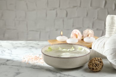 Spa composition with bowl of water and burning candles on white marble table, space for text