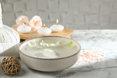 Spa composition with bowl of water and burning candles on white marble table, closeup