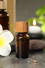 Photo of Spa composition with bottles of cosmetic products, plumeria flower and burning candle on grey table, closeup