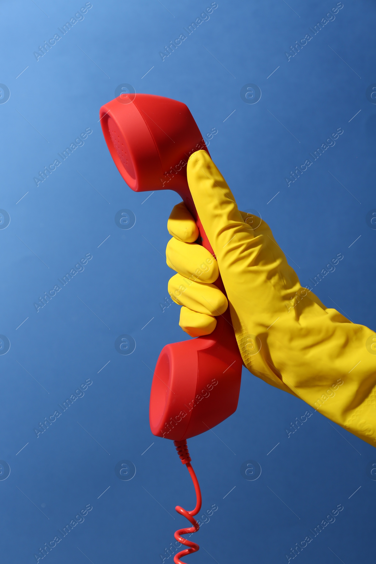 Photo of Woman in rubber glove holding red telephone handset on blue background, closeup