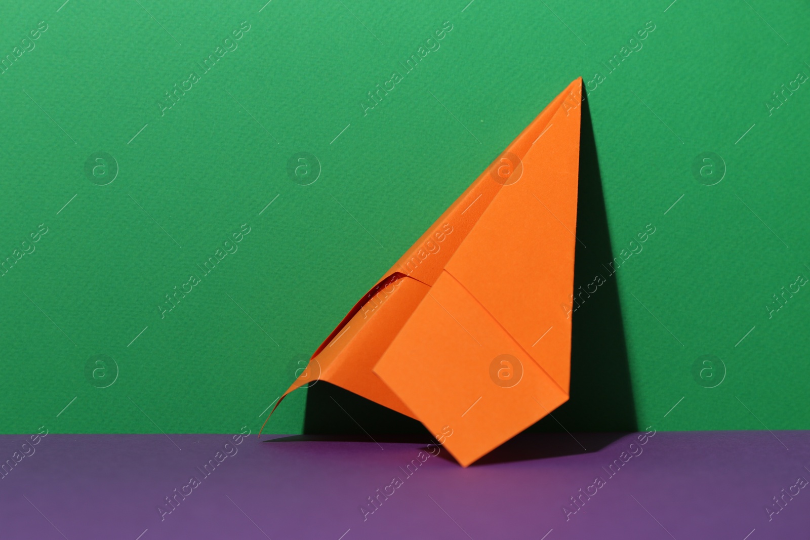 Photo of Handmade orange paper plane on color background