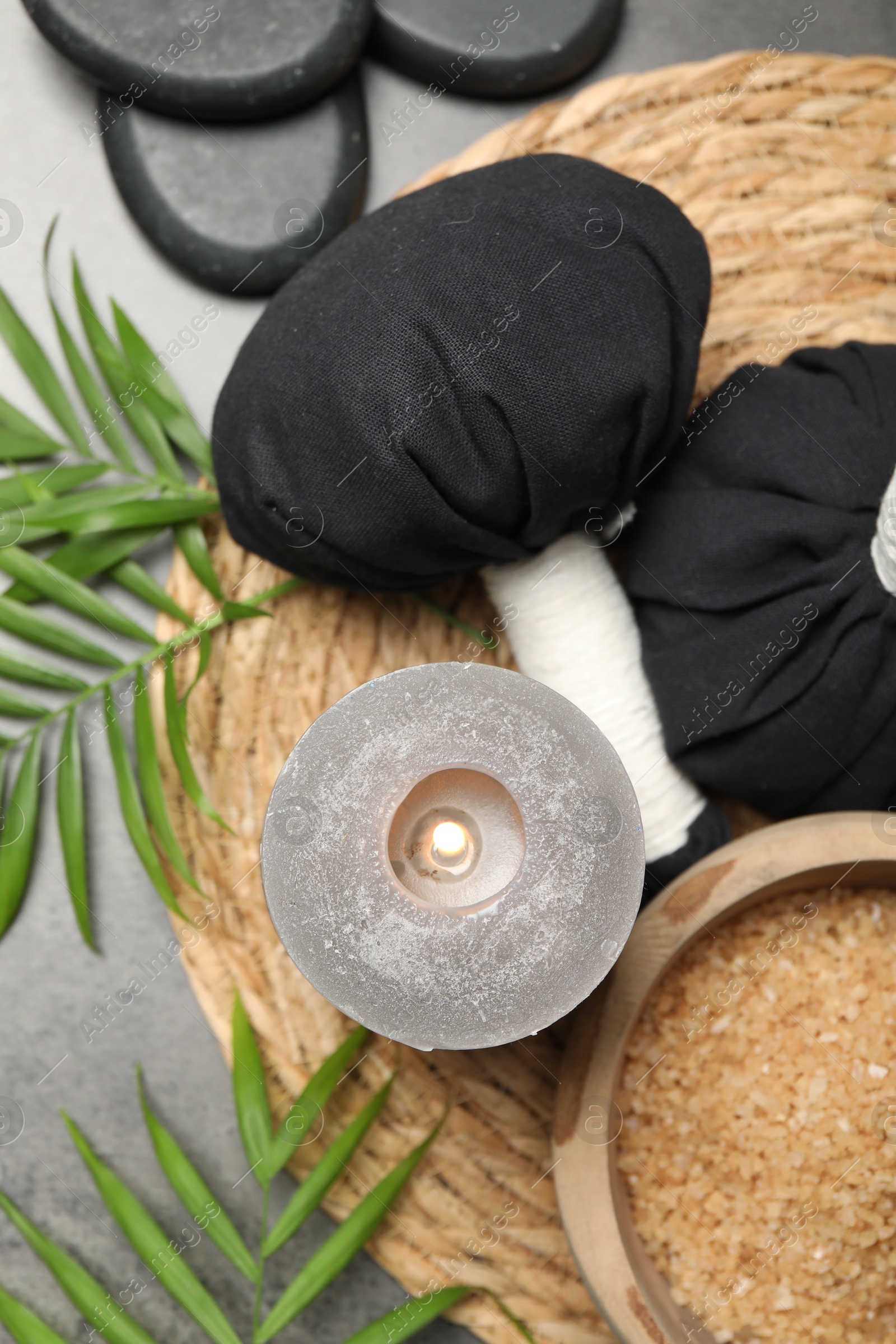 Photo of Spa composition with herbal bags and burning candle on grey table, flat lay