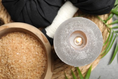 Spa composition with herbal bags and burning candle on grey table, flat lay