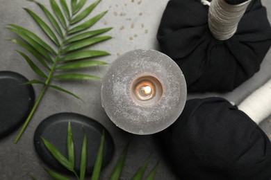 Spa composition with herbal bags and burning candle on grey table, flat lay