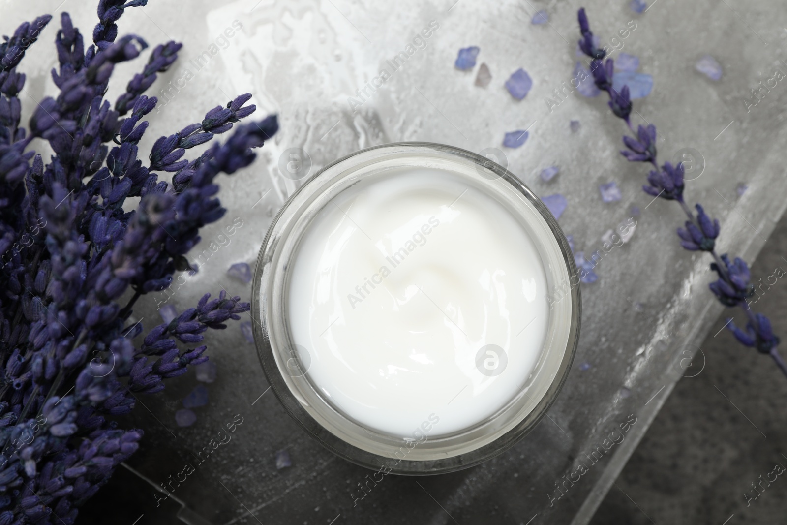 Photo of Spa composition with jar of cosmetic product and lavender flowers on grey table, flat lay