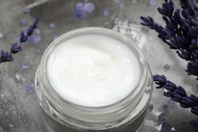 Spa composition with jar of cosmetic product and lavender flowers on grey table, closeup