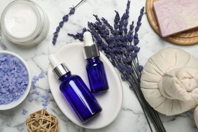 Spa composition with different cosmetic products, herbal bags and lavender flowers on white marble table, flat lay