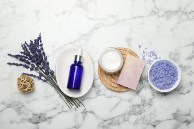 Spa composition with different cosmetic products and lavender flowers on white marble table, flat lay