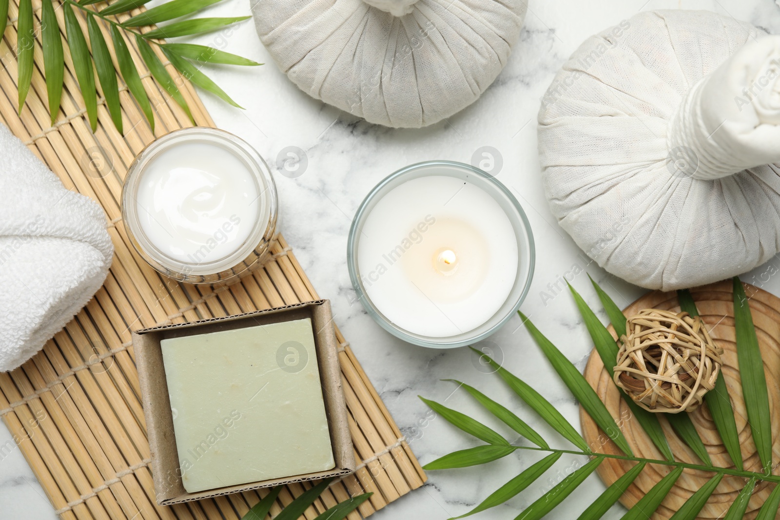 Photo of Spa composition with different cosmetic products, herbal bags, burning candle and leaves on white marble table, flat lay