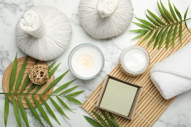 Spa composition with different cosmetic products, herbal bags, burning candle and leaves on white marble table, flat lay