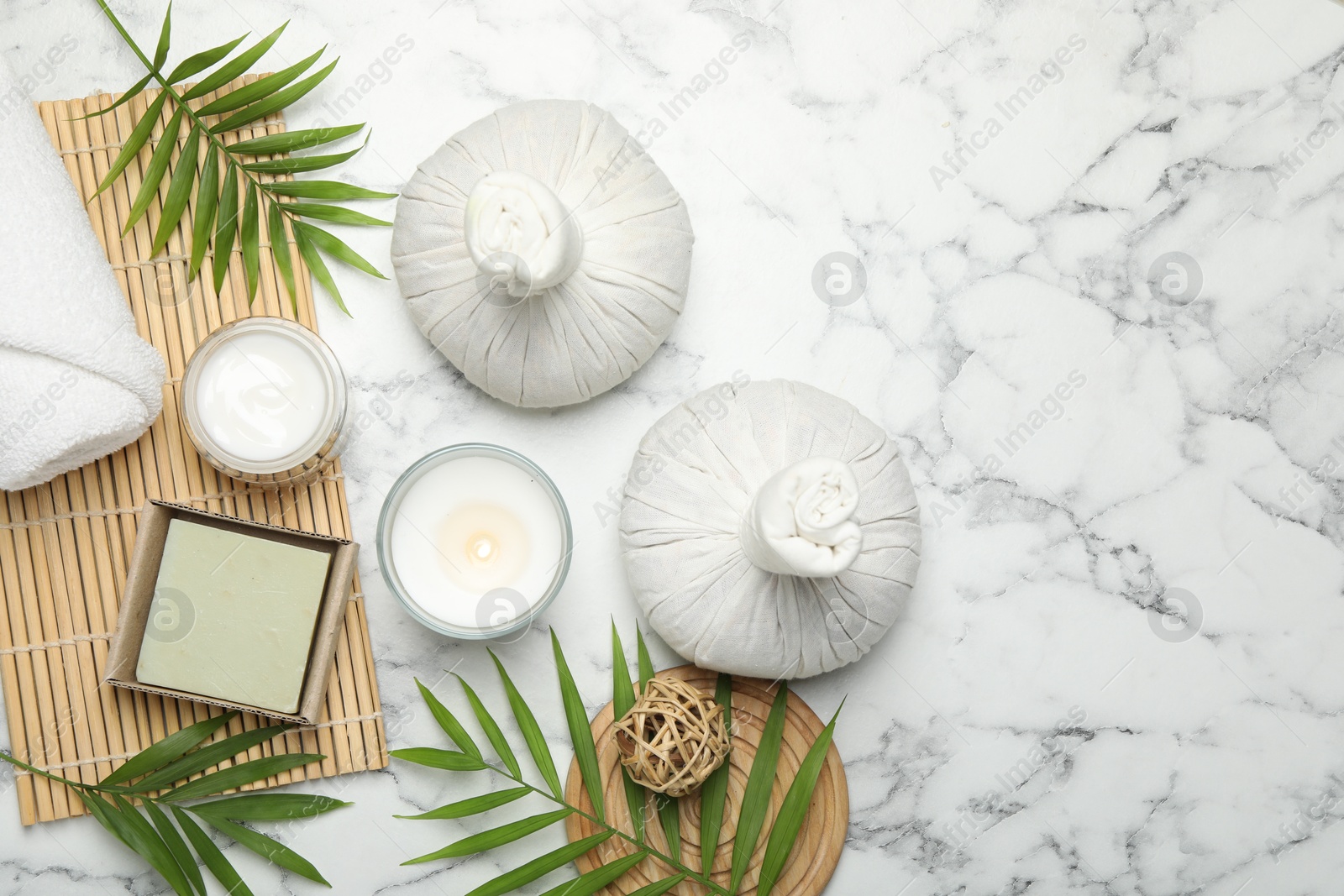 Photo of Spa composition with different cosmetic products, herbal bags, burning candle and leaves on white marble table, flat lay