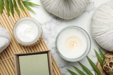 Spa composition with different cosmetic products, herbal bags, burning candle and leaves on white marble table, flat lay