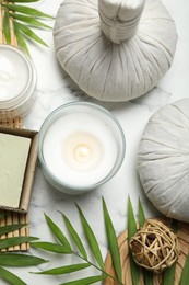 Photo of Spa composition with different cosmetic products, herbal bags, burning candle and leaves on white marble table, flat lay