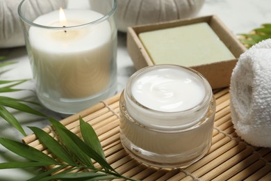 Photo of Spa composition with different cosmetic products, burning candle and leaves on white marble table, closeup