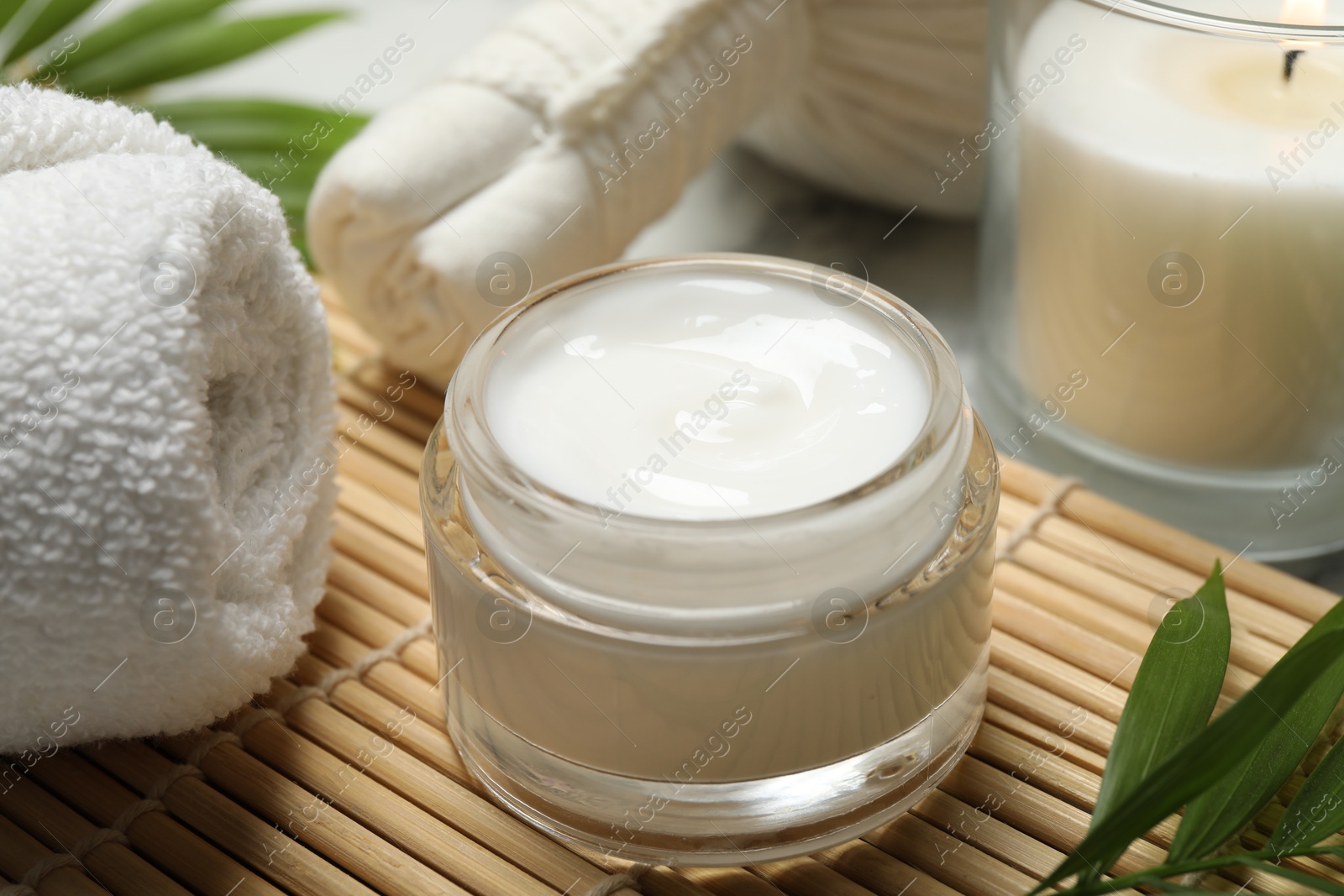 Photo of Spa composition with different cosmetic products, burning candle and leaves on white marble table, closeup