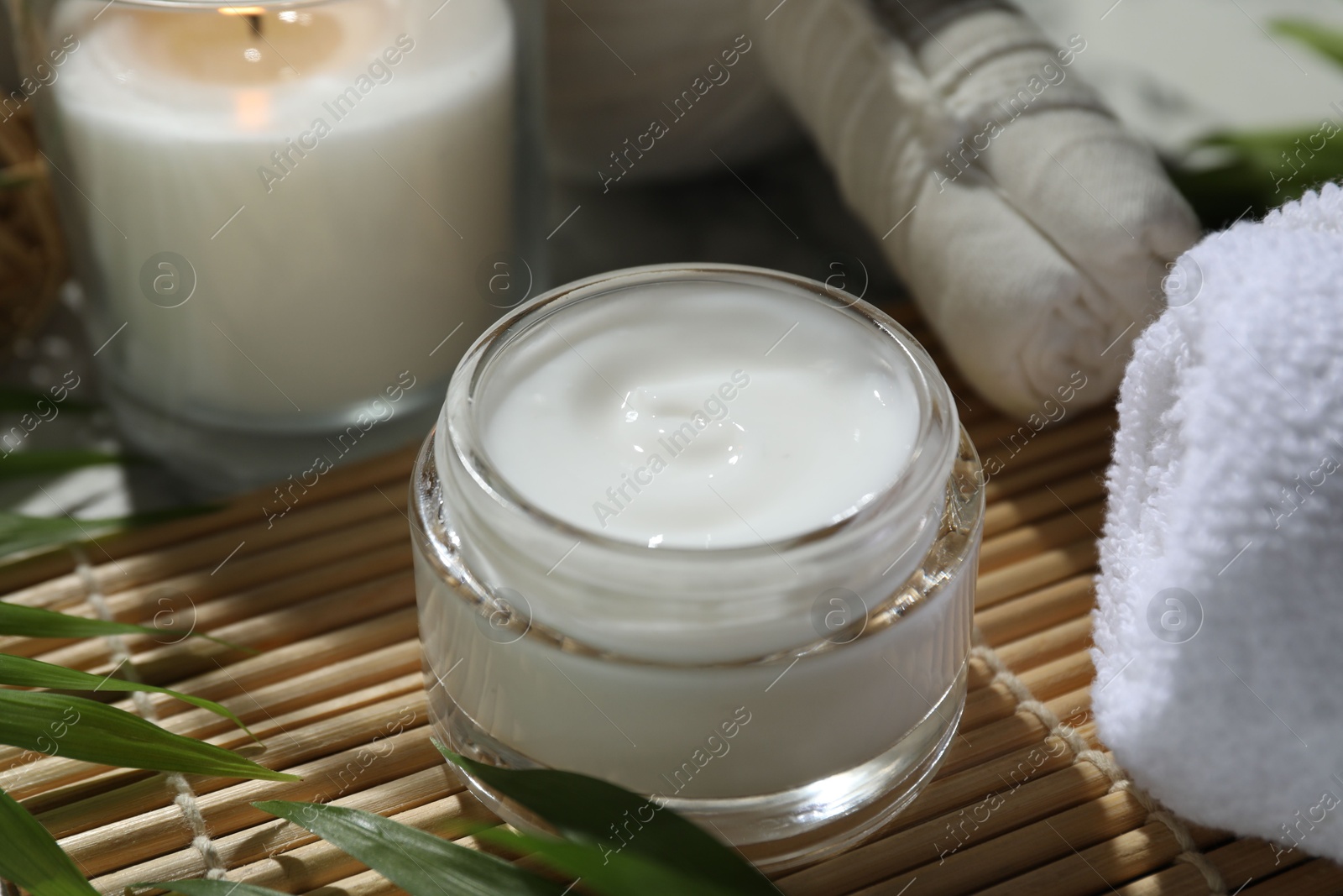 Photo of Spa composition with different cosmetic products, herbal bags, burning candle and leaves on table, closeup