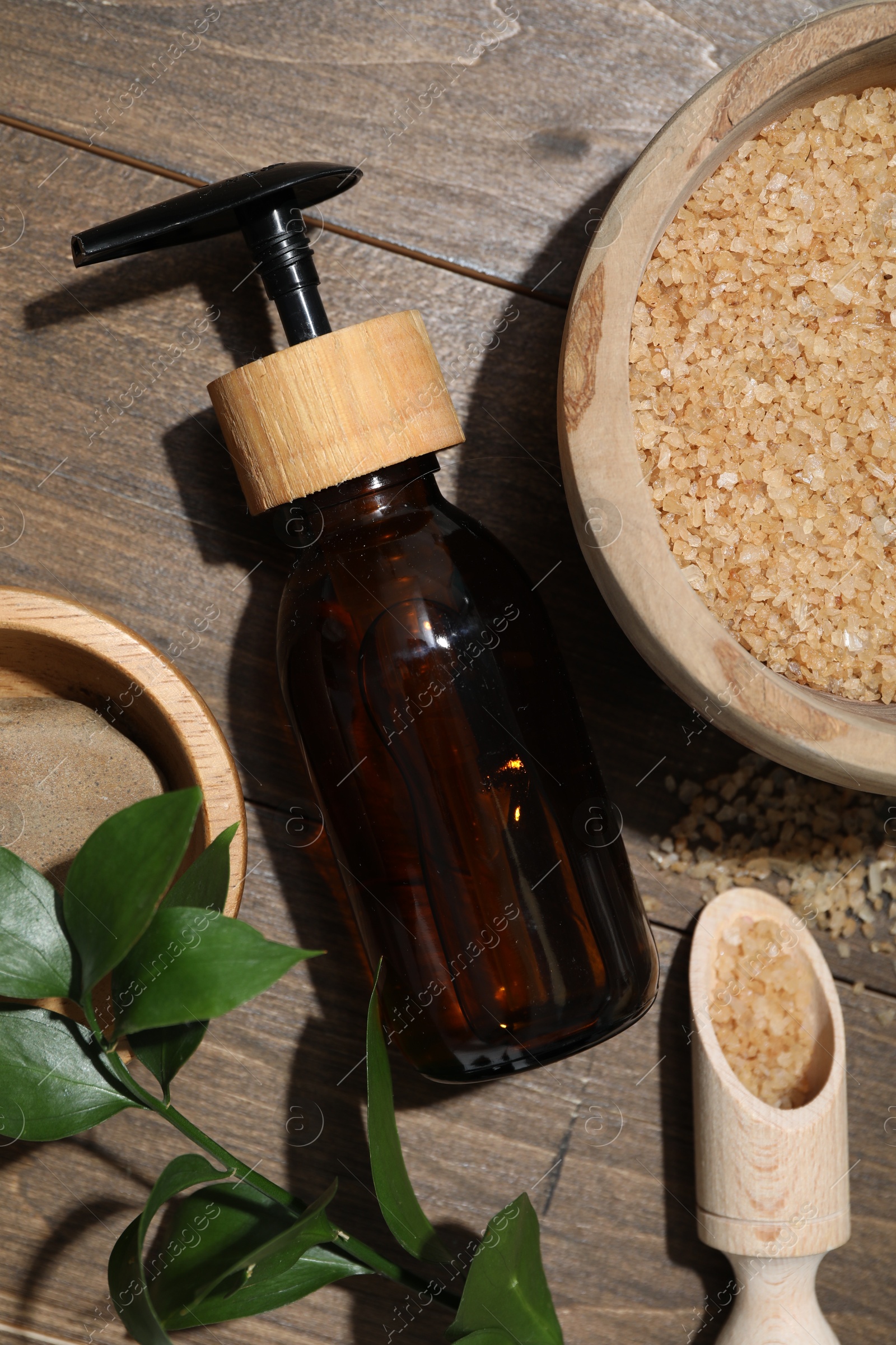 Photo of Spa composition with sea salt, bottle of cosmetic product and leaves on wooden table, flat lay