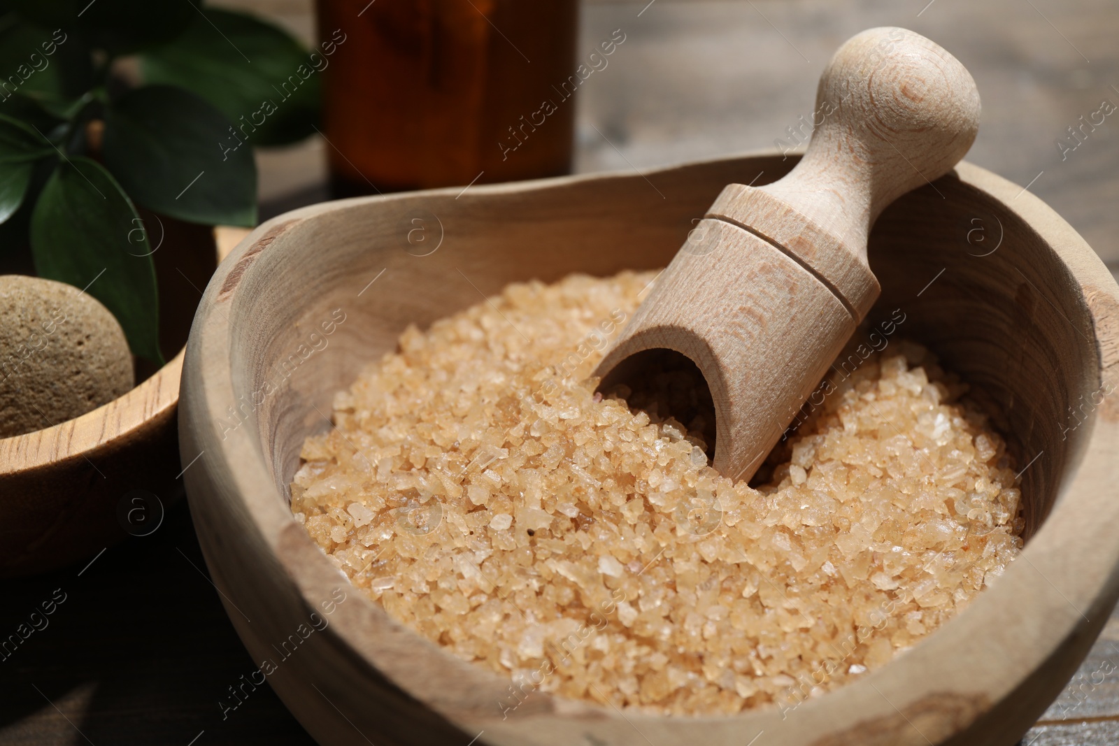 Photo of Bowl with sea salt and leaves on wooden table, closeup. Spa treatment